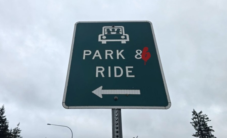 A park and ride sign with a 6 spray painted over the trailing edge of the ampersand